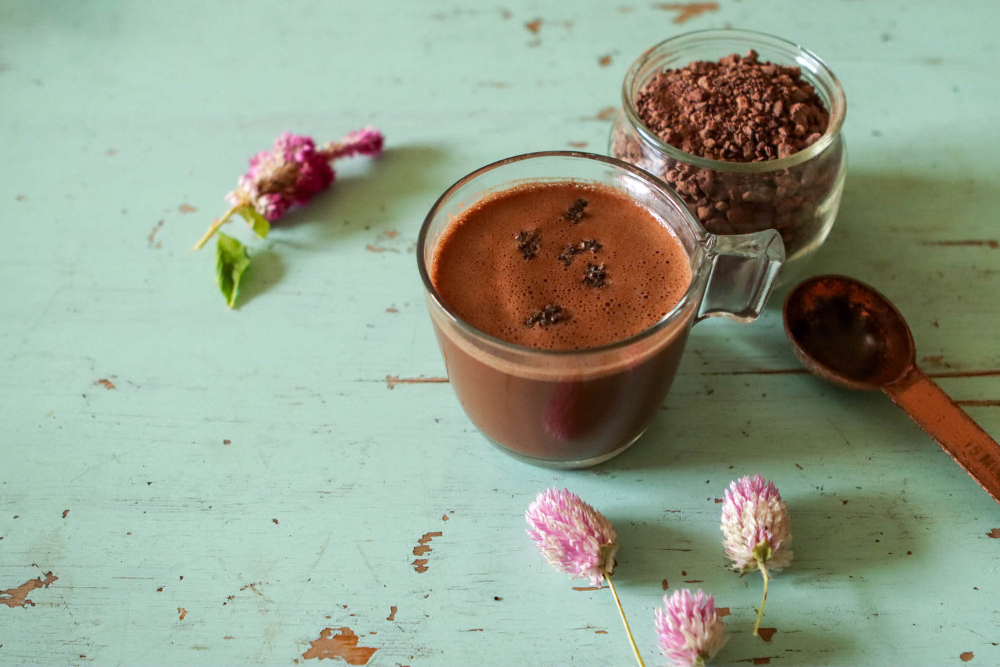 Cup of Ceremonial Cacao with purple flowers on a green table