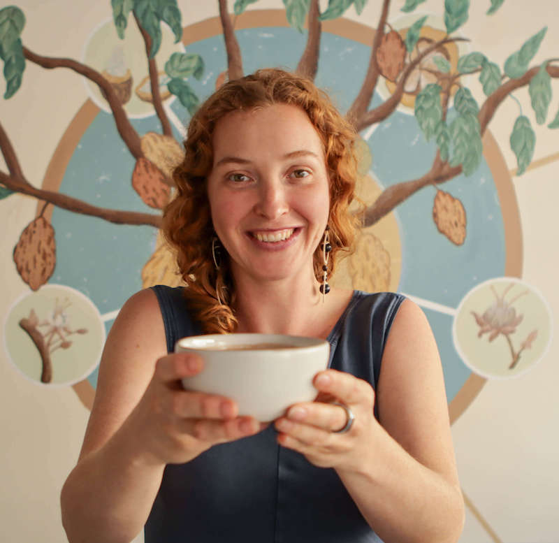 woman smiling while holding out a bowl of ceremonial-grade cacao
