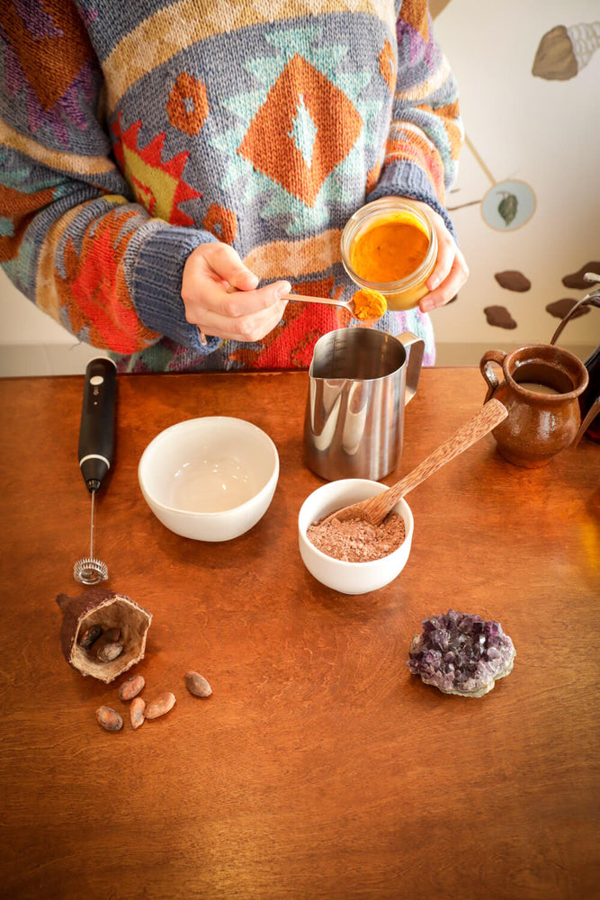 Woman adding yellow turmeric to ceremonial cacao drink