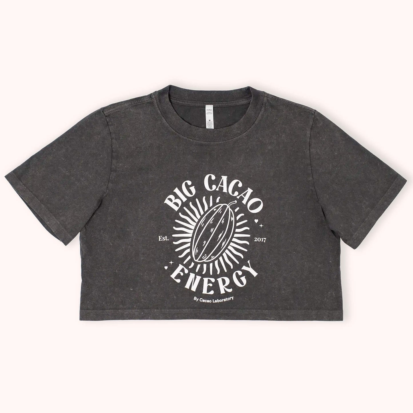 A dark gray cropped t-shirt with a white graphic print reading 'BIG CACAO ENERGY' and featuring a cacao pod illustration, laid flat against a light cream background.