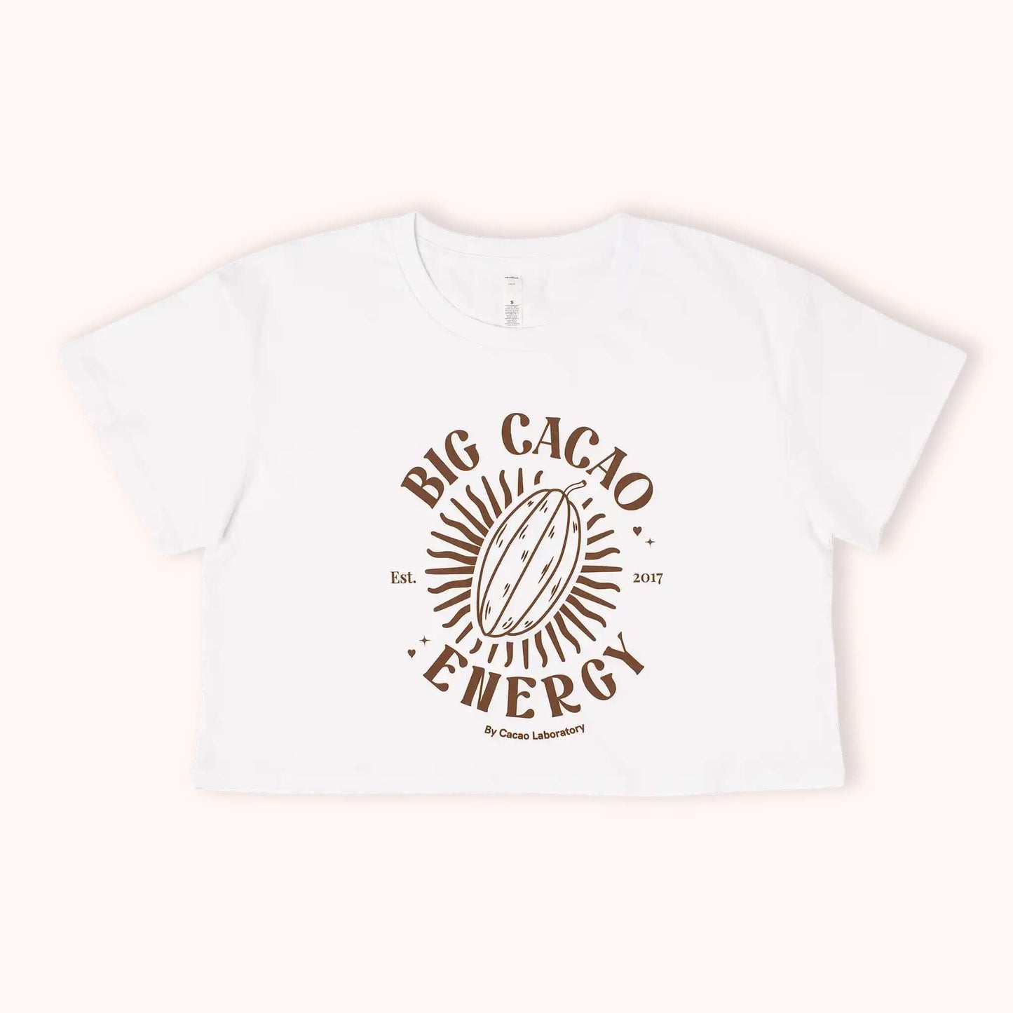 A white short-sleeve cropped T-shirt with a brown graphic print reading 'BIG CACAO ENERGY' around a cacao pod illustration, shown on a light cream background.