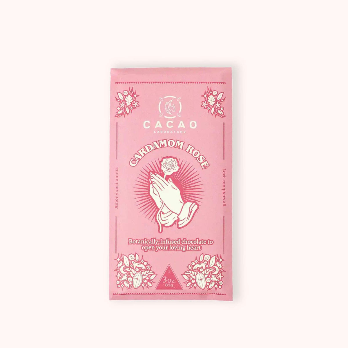 A pink chocolate bar package labeled 'Cacao Laboratory' and 'Cardamom Rose' with floral illustrations and a central praying hands rose graphic, centered on a light cream background.