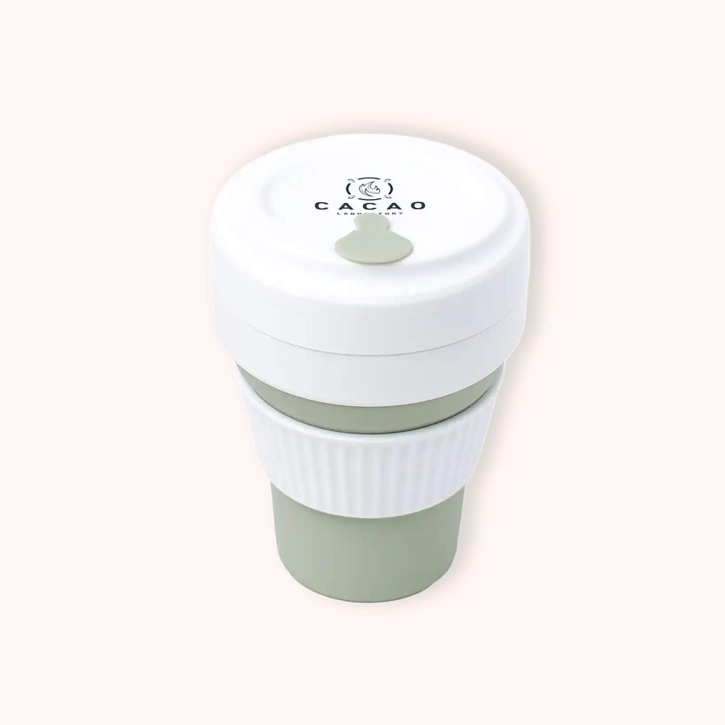 A reusable collapsible travel cup with a white lid and handle, and a muted sage green body, shown on a plain light beige background. The lid is printed with the brand name 'CACAO'.