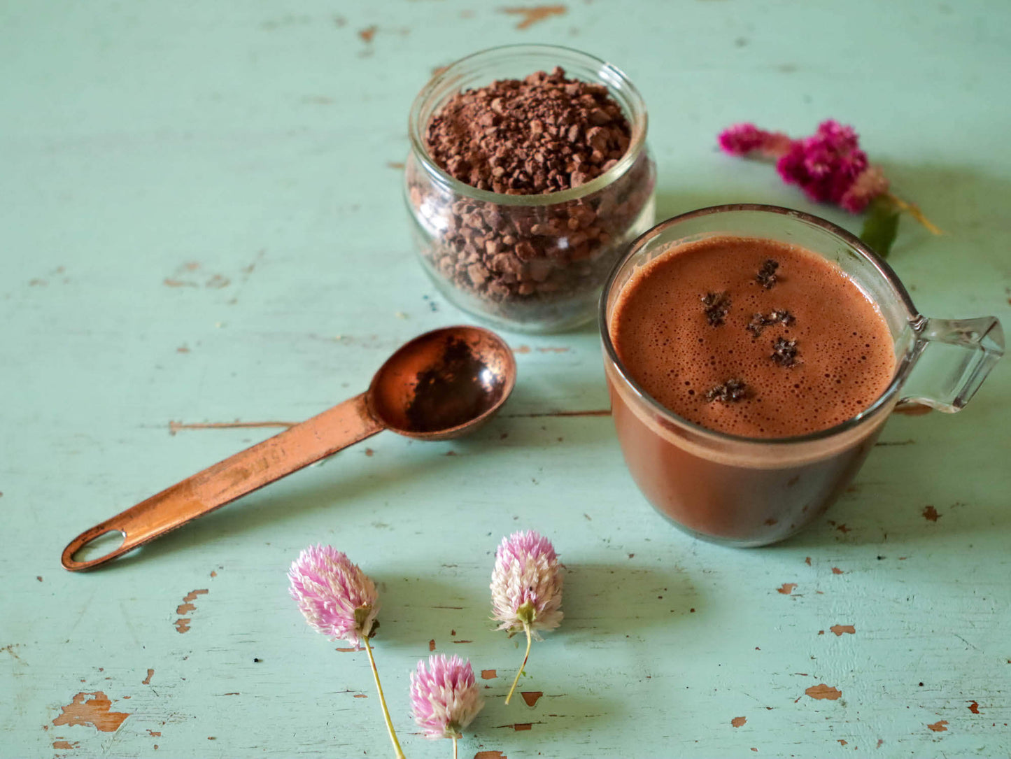 Cup of Ceremonial Cacao with purple flowers on a green table