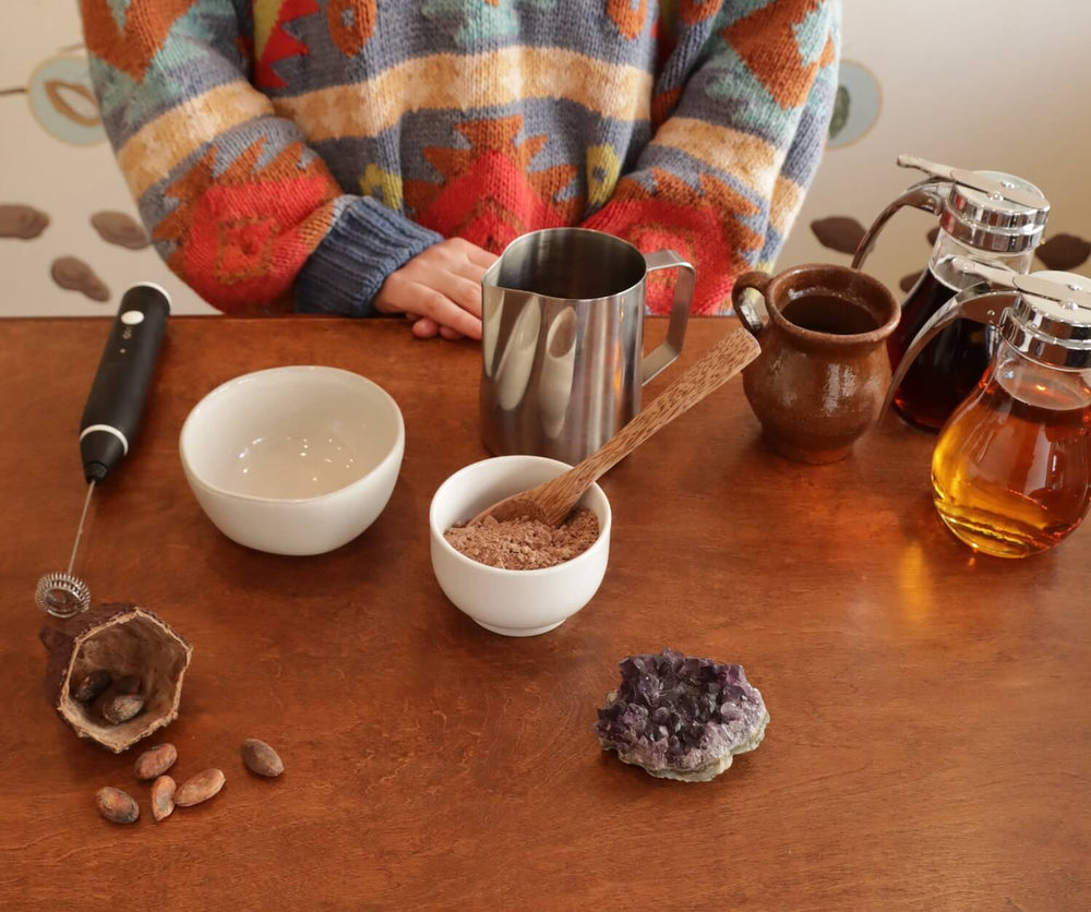place setting for a drink with cocoa, maple syrup, a cup, and a mixing vessel
