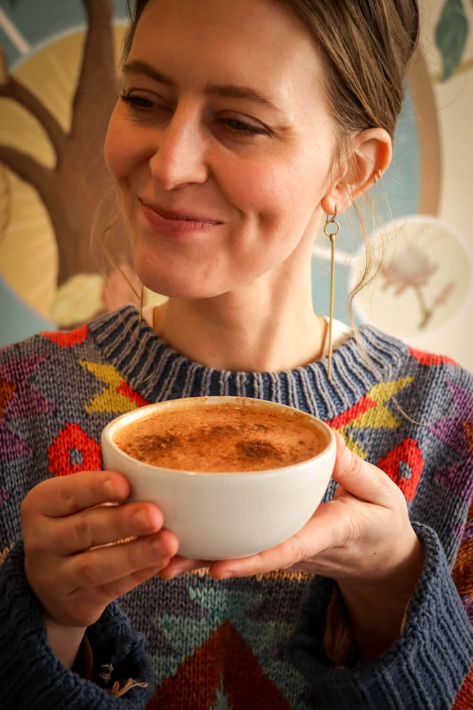 A woman in a colorful sweater enjoying a frothy cup of ceremonial cacao