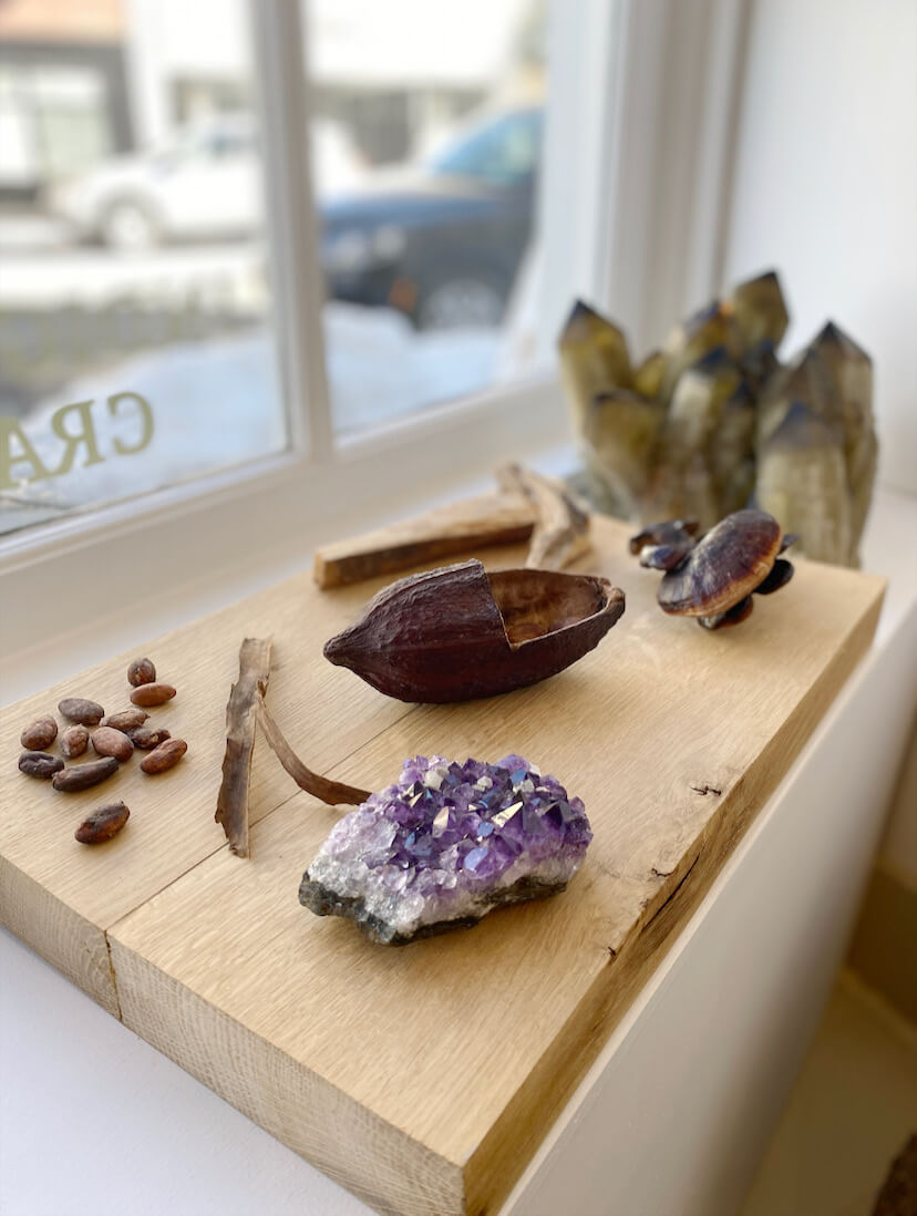 wooden board in a window with crystals, cacao pods and beans, and mushrooms