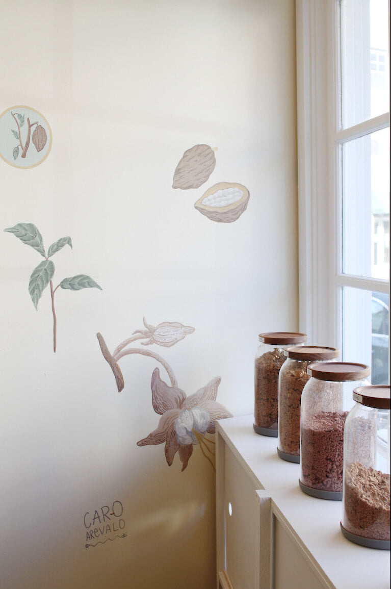 Jars of ceremonial cacao by a window with a cacao mural in the background