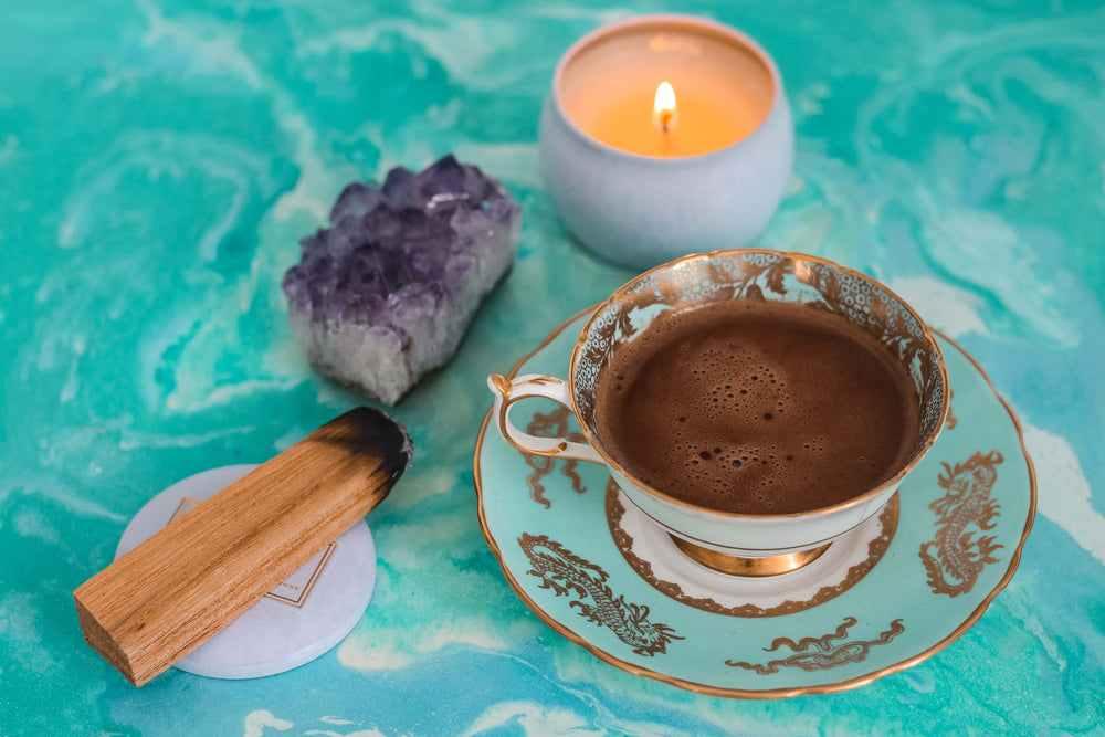 A cup of cacao in a decorative cup with a crystal and a palo santo stick