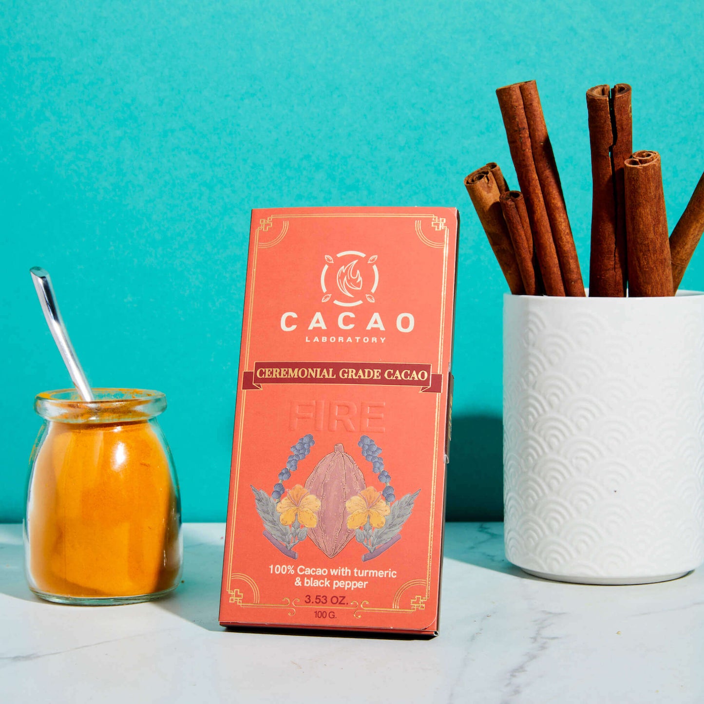 Cacao Laboratory ceremonial grade cacao packaging with cinnamon sticks and a jar of turmeric on a teal background